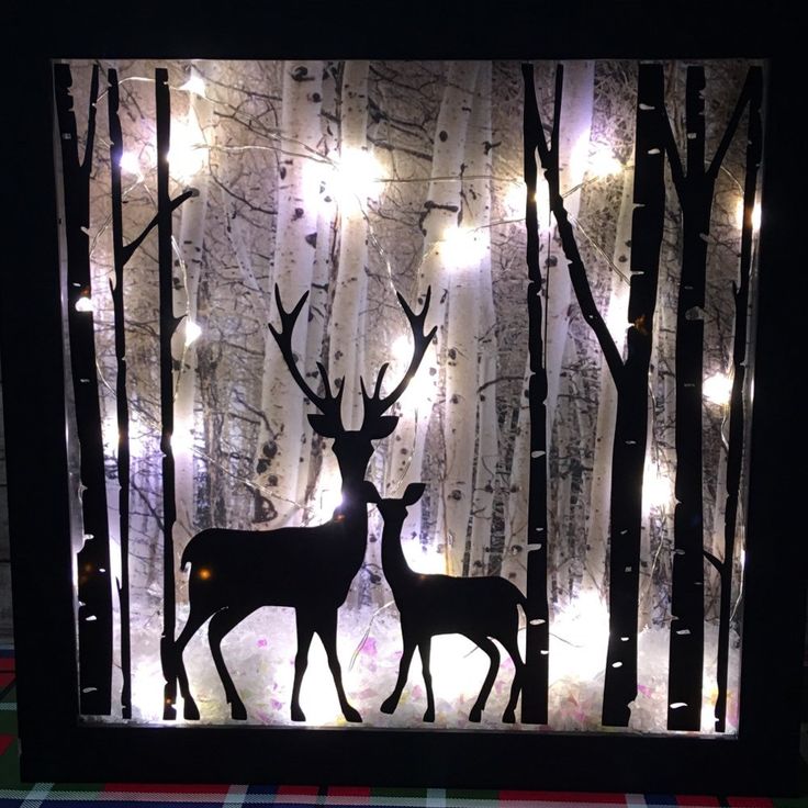 two deer standing in front of a forest with lights