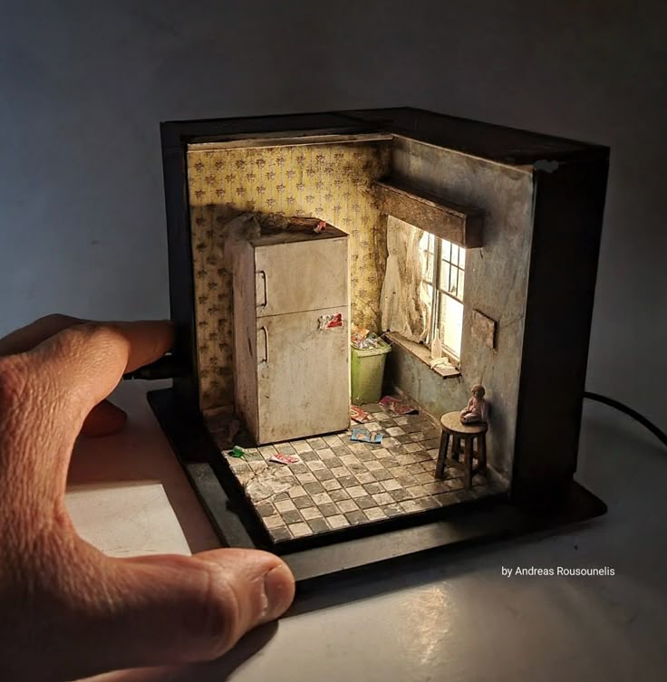 a hand is holding up a miniature model of a doll's house with the door open