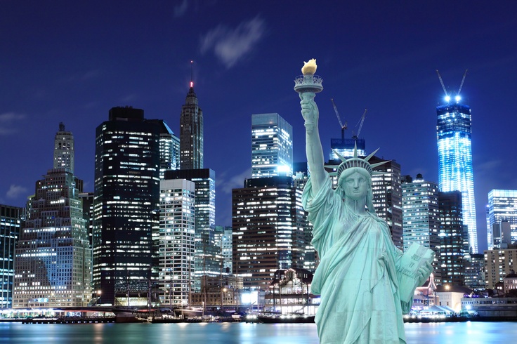 the statue of liberty is lit up at night in new york city, with skyscrapers behind it