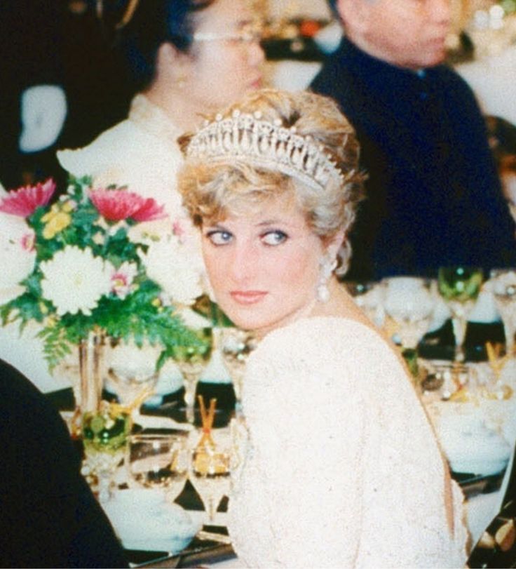 the princess is wearing a tiara and sitting at a table with other people around her