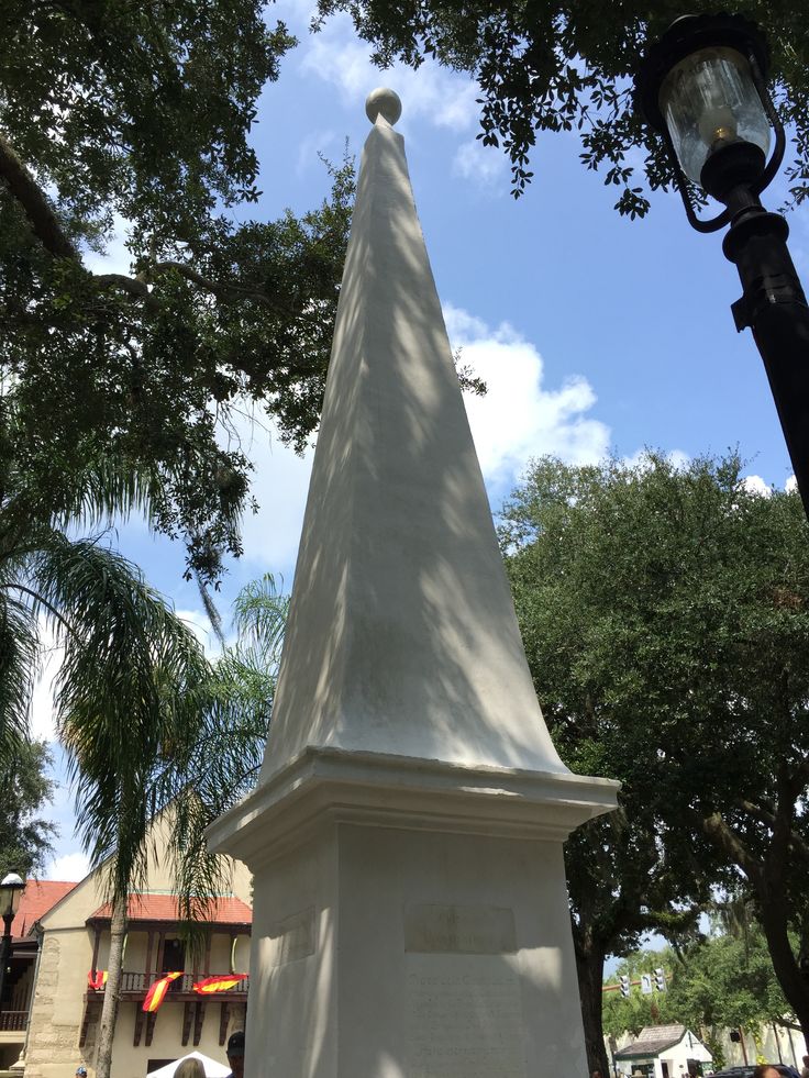 a large white monument with a clock on it's side in front of some trees