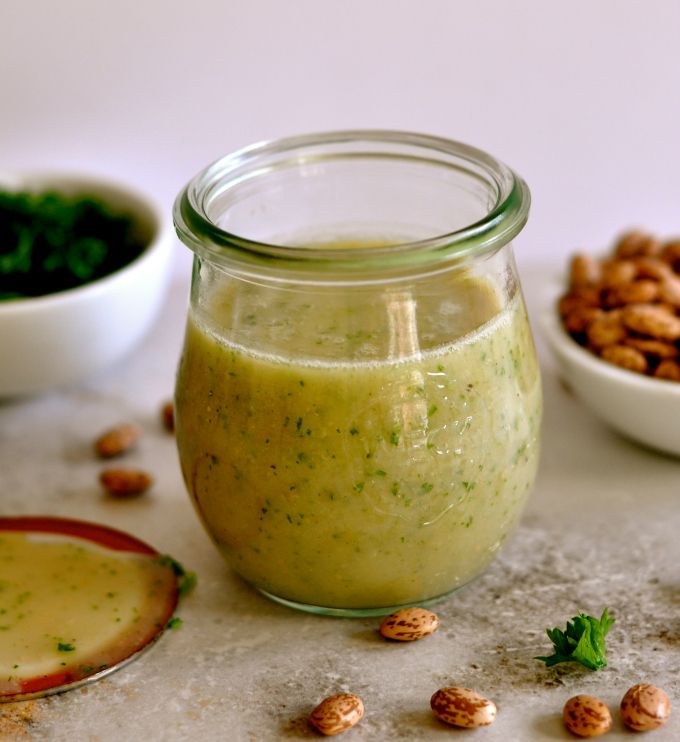 a glass jar filled with green liquid next to nuts