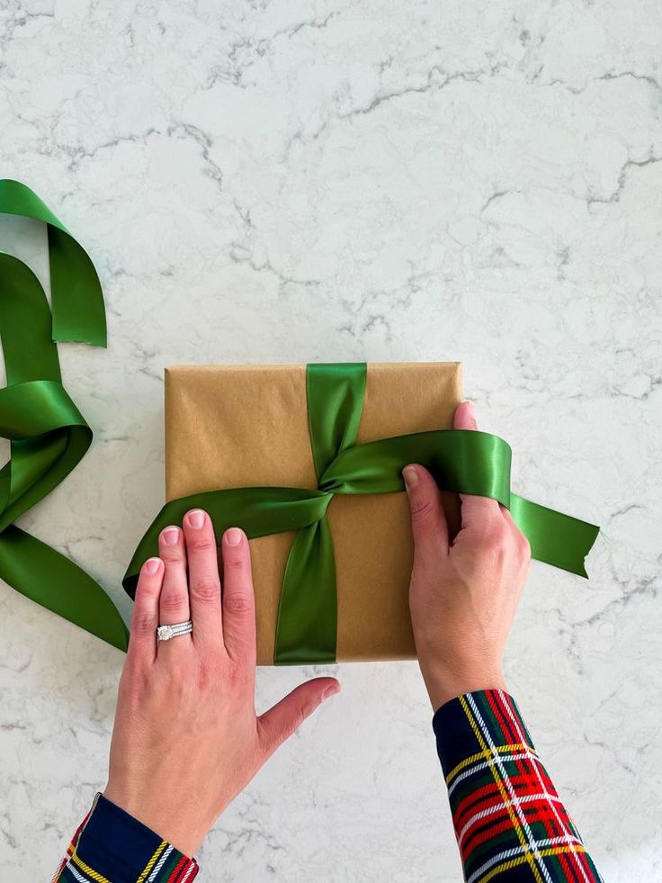 two hands holding a wrapped present box with green ribbon on it and another person's hand next to it