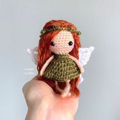 a hand holding a tiny crocheted doll with red hair and angel wings on it's finger