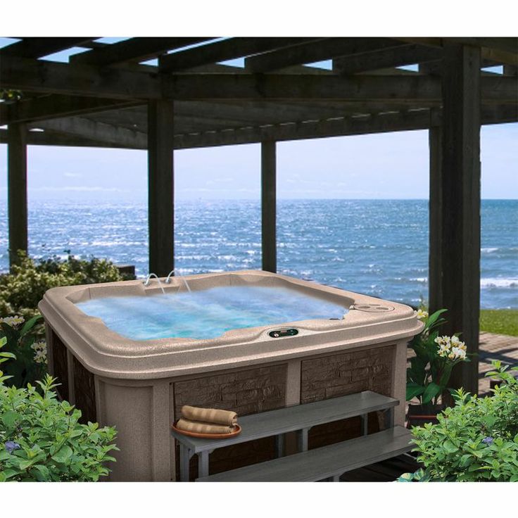 a large hot tub sitting on top of a wooden deck next to the ocean in front of a pergolated gazebo