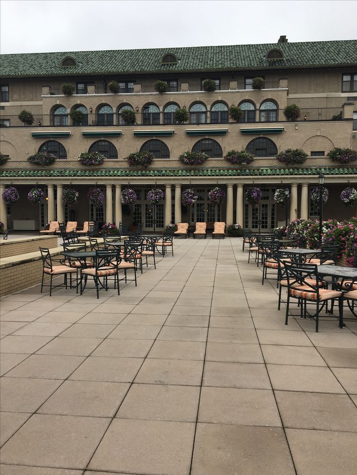 tables and chairs in front of a large building with flowers growing on the side of it