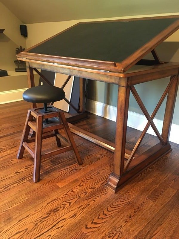 a wooden desk with a black top and two stools next to it on a hard wood floor