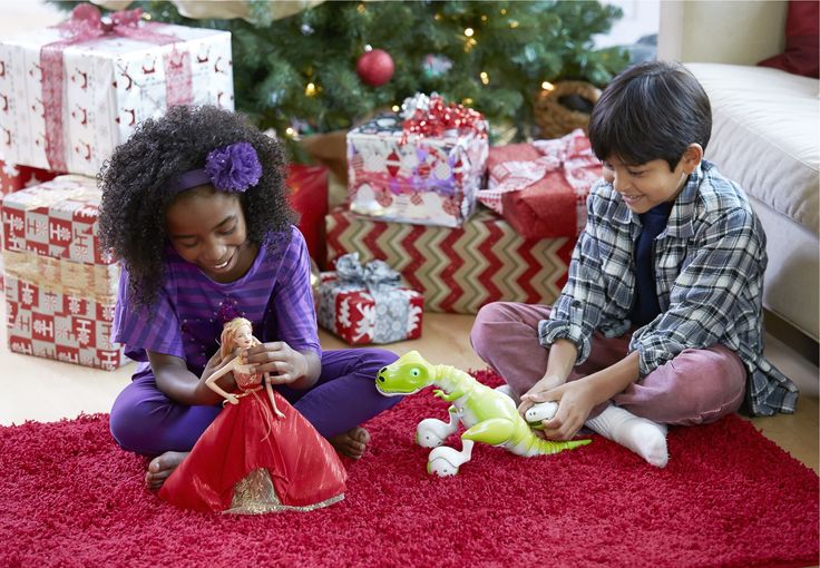 two children are playing with toys in front of a christmas tree and presents on the floor