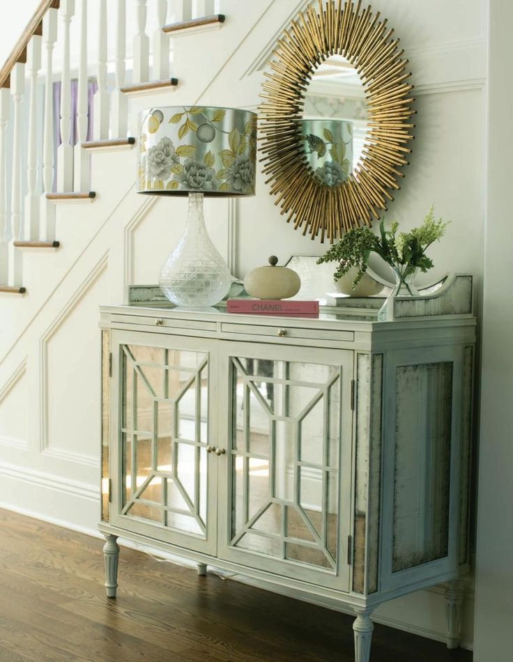 a white cabinet with a mirror on top of it next to a stair case and table lamp