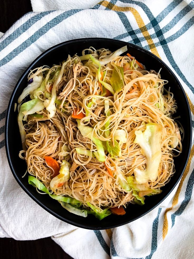 a pan filled with noodles and vegetables on top of a white towel next to a fork