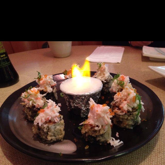 a black plate topped with sushi and a lit candle on top of a table