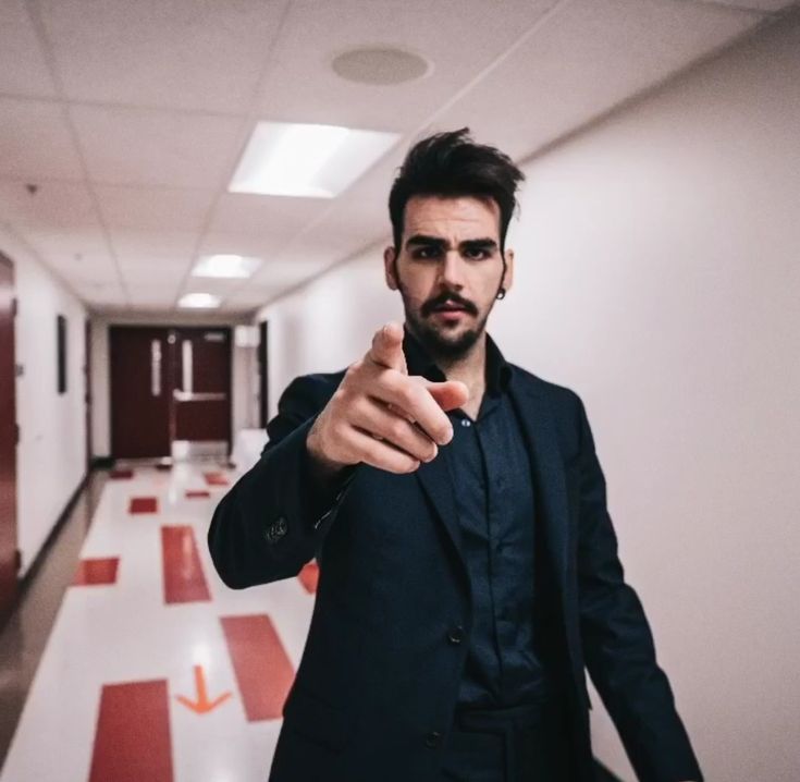 a man pointing his finger at the camera in an empty hallway with red and white tiles on the floor