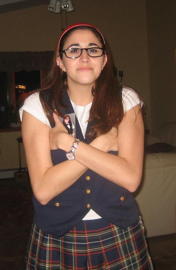 a woman wearing glasses and a kilt is standing with her arms crossed in front of her chest