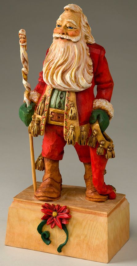 a santa clause figurine holding a stick on top of a wooden block with a poinsetti