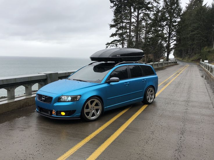 a blue car with a surfboard strapped to it's roof on the road