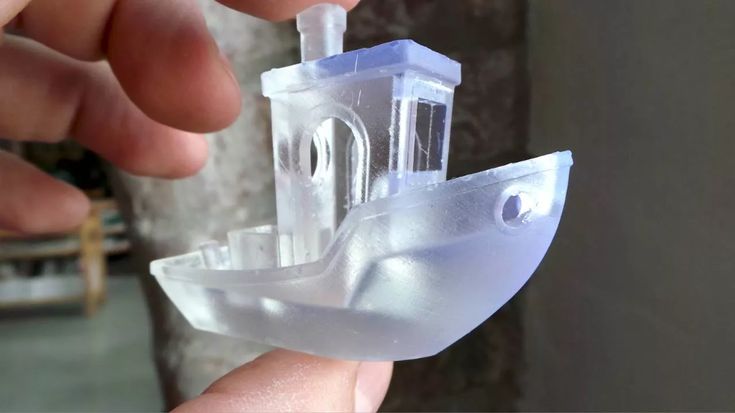 a plastic model of a boat being held by a person's hand in front of a tree