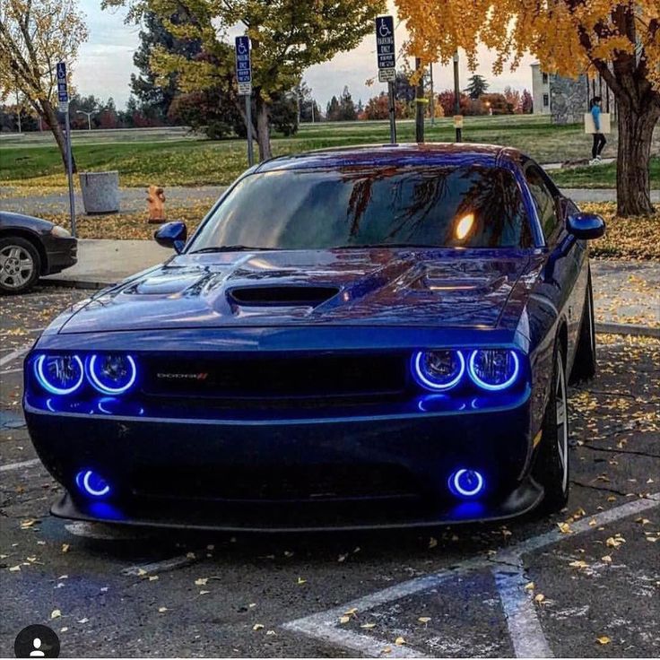 a blue dodge car parked in a parking lot next to a tree with yellow leaves