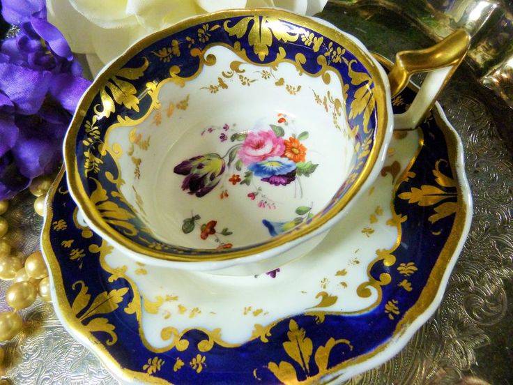 a tea cup and saucer sitting on top of a table next to purple flowers