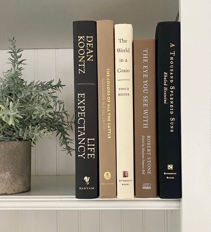 three books are sitting on a shelf next to a potted plant in the corner