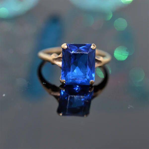 A ladies 10 karat yellow gold "Helm & Hahn" ring set with an 8 by 10 millimeter rectangular synthetic blue spinel.  The ring is size 6 Blue Sapphire Emerald Cut Promise Ring, Blue Sapphire Crystal Ring For Formal Occasions, Blue Emerald Cut Birthstone Ring With Prong Setting, Formal Blue Sapphire Crystal Ring, Blue Emerald Cut Ring, Birthstone, Blue Sapphire Birthstone Ring With Emerald Cut, Blue Emerald Cut Ring For Birthstone, Blue Emerald-cut Ring With Birthstone, Blue Emerald Cut Ring With Birthstone