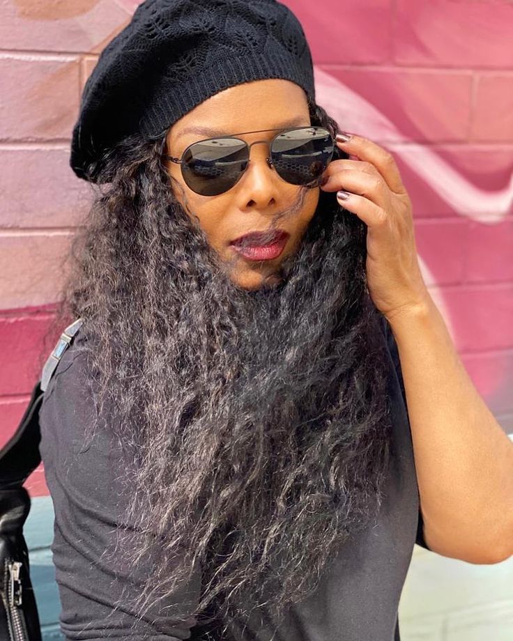 a woman with long grey hair wearing sunglasses and a black beanie on her head