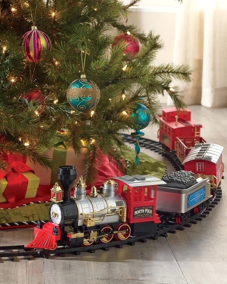 a christmas tree is decorated with ornaments and train tracks in front of a small toy train