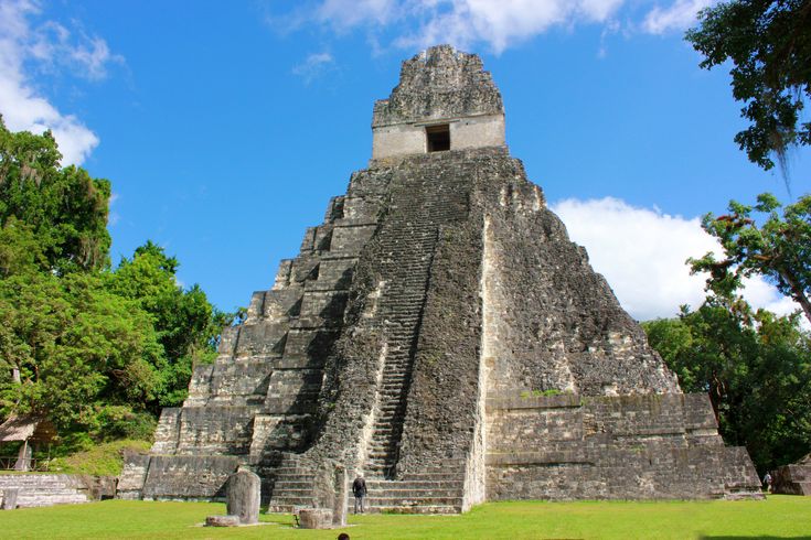 an ancient pyramid in the middle of a park with people walking around and trees surrounding it