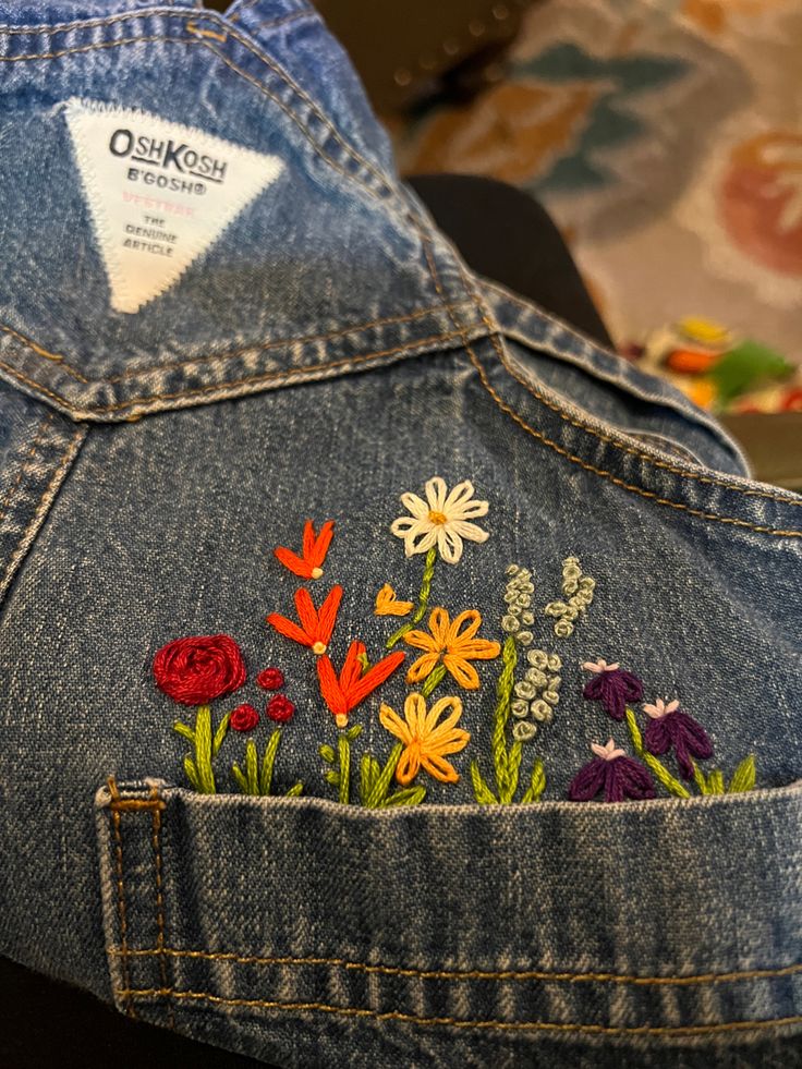 the back of a jean jacket with flowers embroidered on it's side and an ostrich patch in the pocket