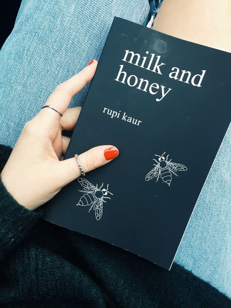 a woman holding up a book about milk and honey in her lap while sitting down