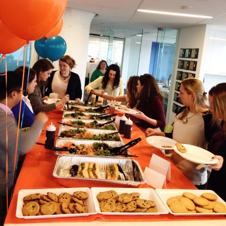 a group of people standing around a table filled with plates and trays of food