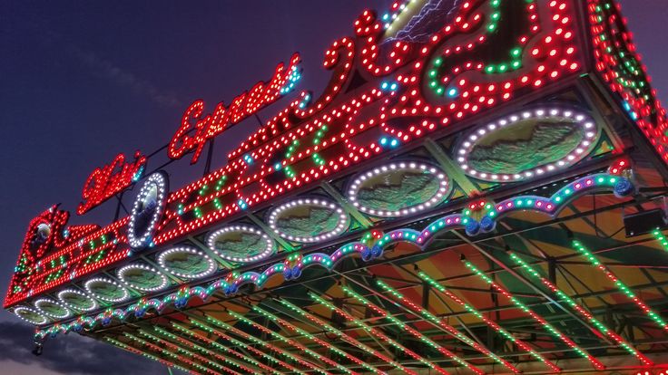 an illuminated merry go round at night with the sky in the backgrouund