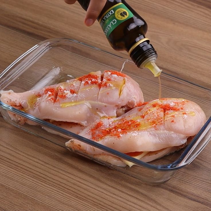 someone is adding seasoning to raw chicken in a glass dish on a wooden table