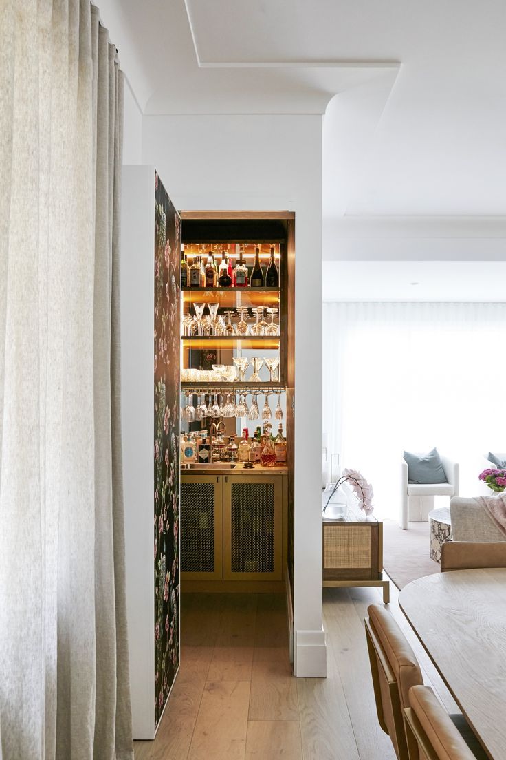 a dining room table and some chairs in front of a wall with bottles on it