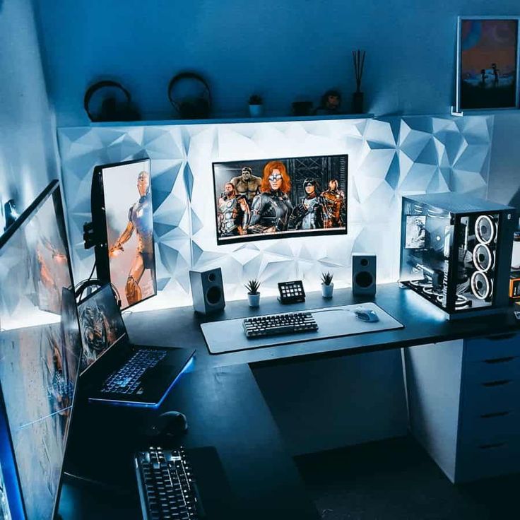 a computer desk with two monitors and speakers on it, in front of a blue wall