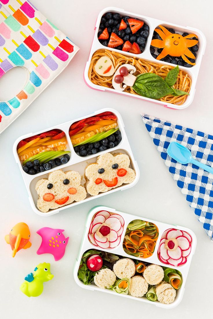 three plastic trays filled with food on top of a white table next to colorful napkins