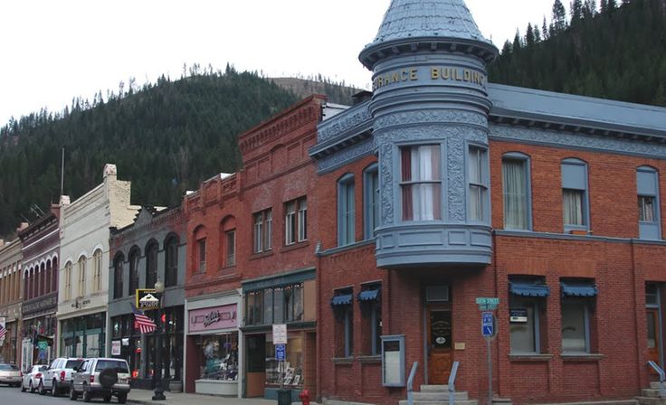 an old fashioned building on the corner of a city street with mountains in the background