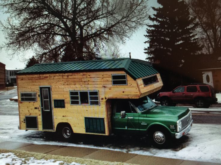 a green truck parked next to a wooden house on top of it's roof