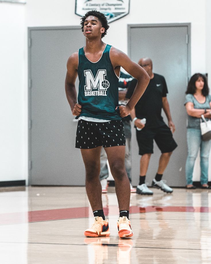 a young man standing on top of a basketball court wearing shorts and a tank top