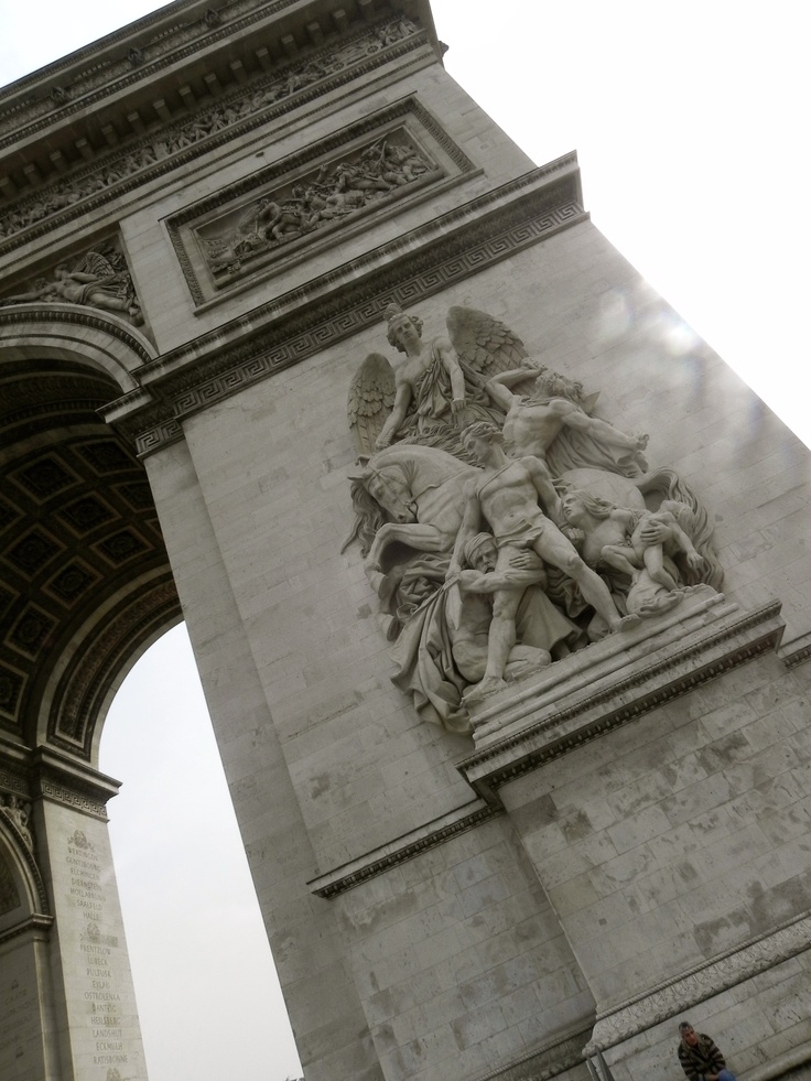 an arch with statues on the sides and people walking around it in front of it