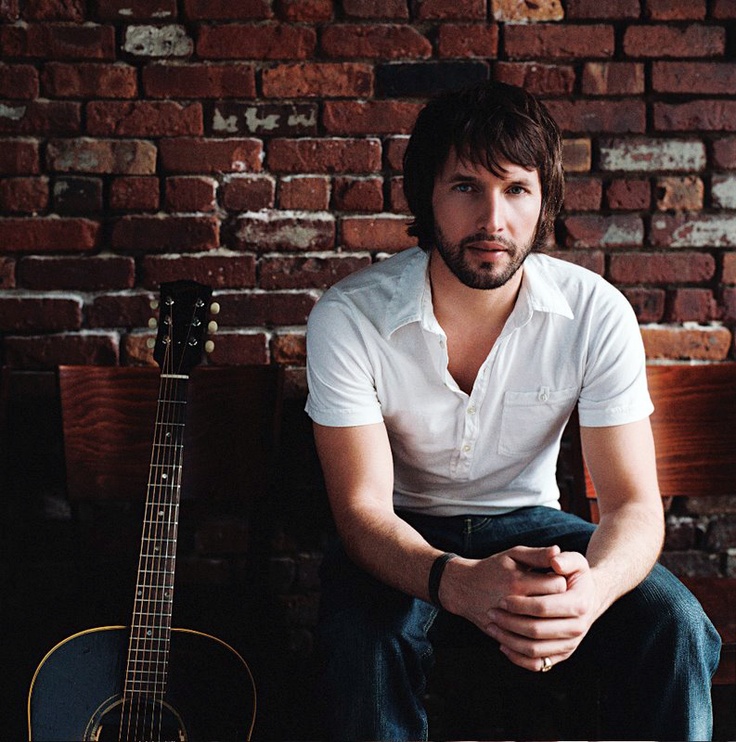 a man sitting on a bench next to a brick wall with an acoustic guitar in front of him