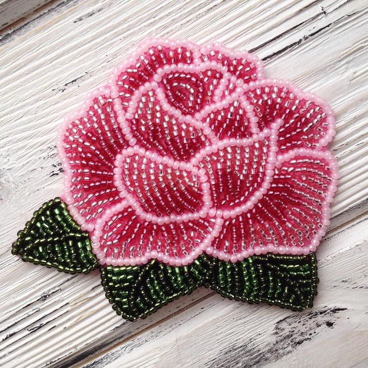 a pink flower with green leaves is on a white wooden surface next to a pair of scissors