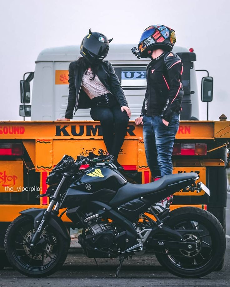 two people sitting on the back of a truck next to a motorcycle