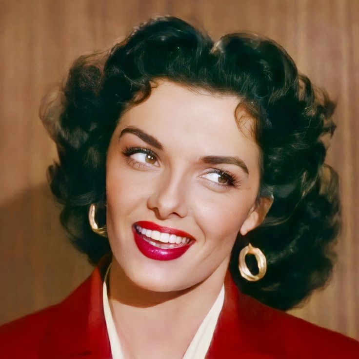 a close up of a person wearing a red suit and smiling with big hoop earrings on her head