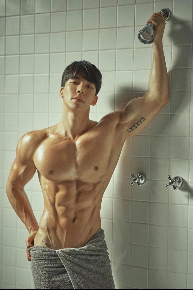 a shirtless man standing in front of a shower with his hands on the wall