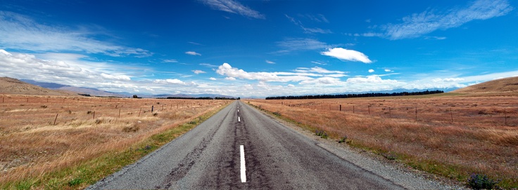 an empty road in the middle of nowhere with blue skies and white clouds above it