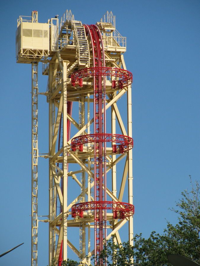 a red and white roller coaster on top of a tall tower with trees in the foreground