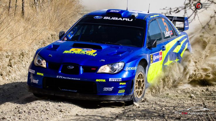 a subaru racing car making a turn on a dirt road with dust coming from behind it