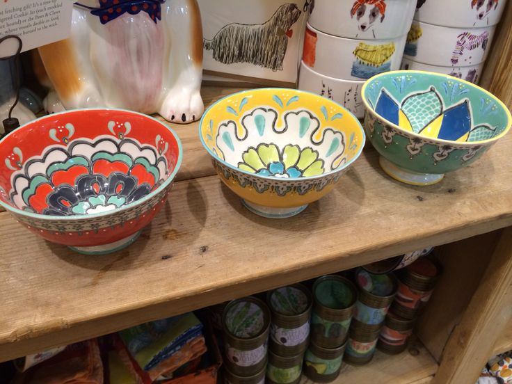 three colorful bowls sitting on top of a wooden shelf