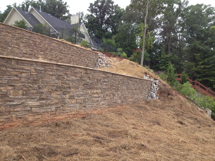 a stone wall next to a hillside with grass growing on it and trees in the background