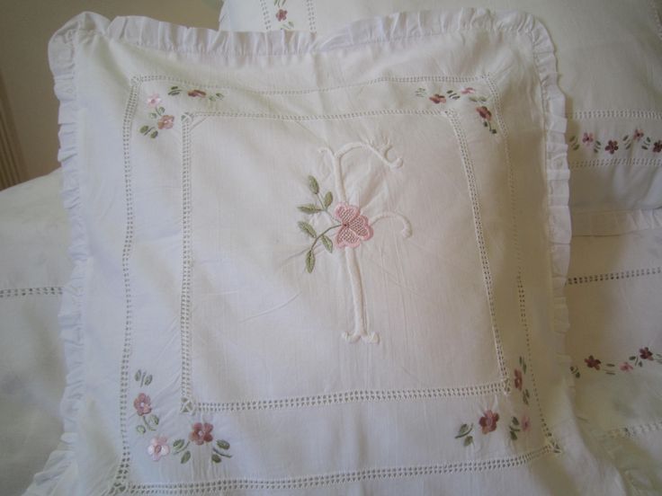 two white pillows with pink flowers and a cross embroidered on them, sitting next to each other